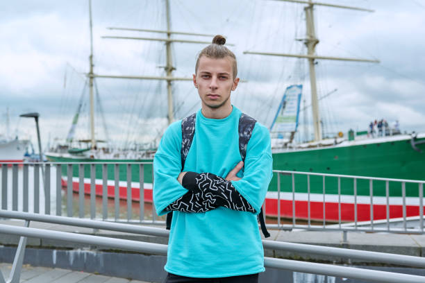 Young guy with backpack with crossed arms outdoor, river port background