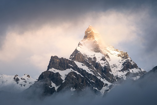 Landscape view of the snowy Cime de l'Est mountain quickly appearing through the dark clouds and illuminated by the rising sun, in Wallis Switzerland