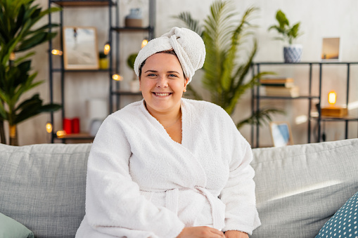 Portrait of a beautiful young plus size woman in a bathrobe sitting on the sofa in the living room.