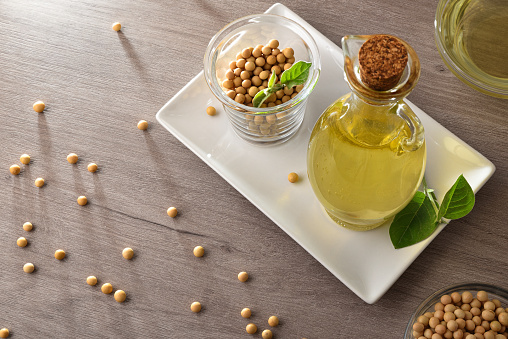 Soybean oil in glass bottle and dry soy beans in white plate on wooden table. Elevated view.