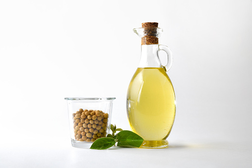 Soybean oil and dry soy beans in glass container and leaves white isolated background. Font view.