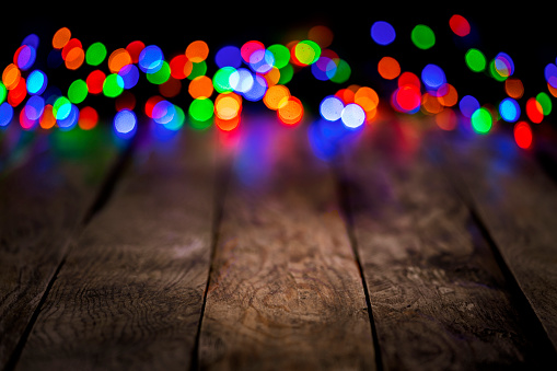 Empty rustic wooden table with blurred multi colored Christmas lights at background