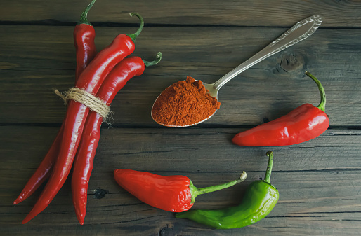 Crushed and whole hot pepper on a wooden table. Chili peppers in pods next to the crushed powder in a spoon.