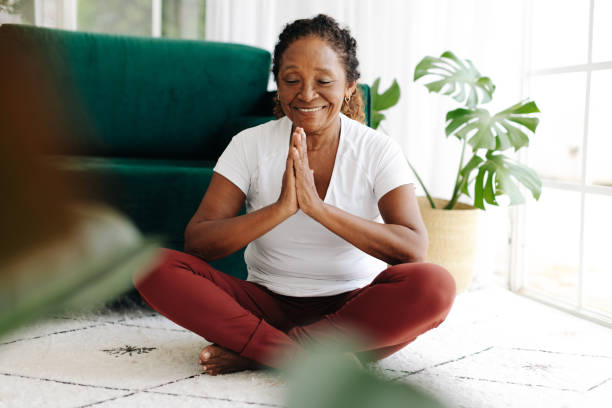 bienestar mental con yoga: mujer mayor meditando en casa - relaxation eyes closed women photography fotografías e imágenes de stock