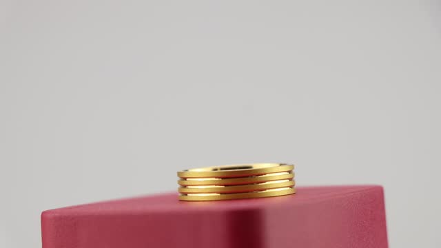 Close up view of a ring made from gold on a rotating movement. Gold ornaments display on a red box