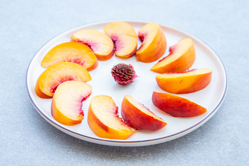 white plate with sliced peaches round shape on grey background, selective focus. Top view