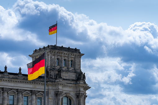 Germany, Berlin, July 04, 2023 -German flags on Berlin Reichstag against dramatic sky Berlin Mitte