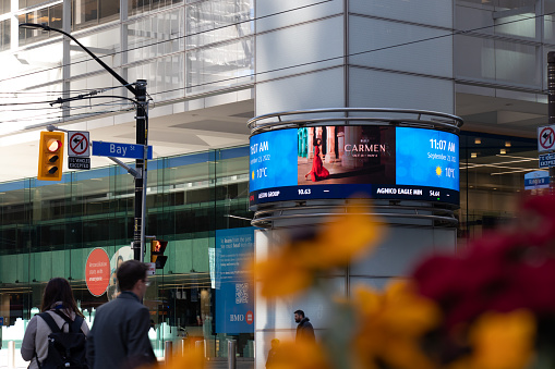 A Bay St. street sign is seen at the base of BMO's First Canadian Place in the Toronto Financial District. as people walk by a TSX digital ticker sign.