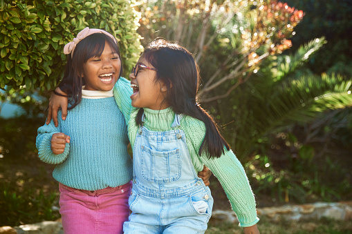 A delightful portrait captures two happy sisters standing side by side in their sunlit garden on a beautiful and sunny day. Their smiles radiate warmth and joy as they share a special moment in the embrace of nature's beauty.