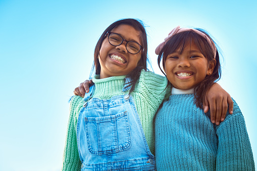 A delightful portrait captures two happy sisters standing side by side in their sunlit garden on a beautiful and sunny day. Their smiles radiate warmth and joy as they share a special moment in the embrace of nature's beauty.