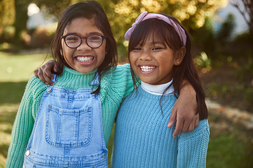 A delightful portrait captures two happy sisters standing side by side in their sunlit garden on a beautiful and sunny day. Their smiles radiate warmth and joy as they share a special moment in the embrace of nature's beauty.