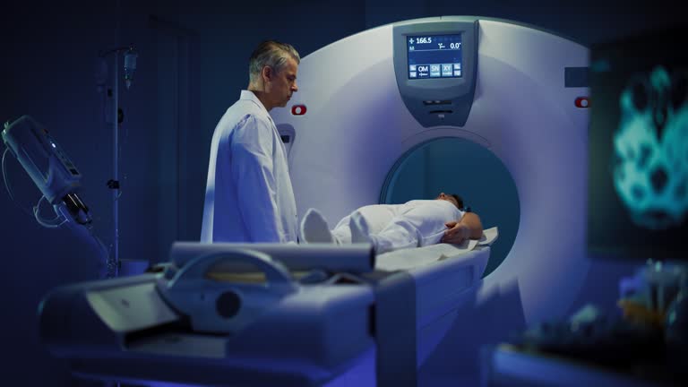 In Medical Laboratory Male Radiologist Controls MRI or CT or PET Scan with Female Patient Undergoing Procedure. High-Tech Modern Medical Equipment. Footage In Medical Laboratory or Healthcare Facility