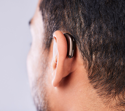 Ear, deaf and hearing aid closeup in studio on a gray background for sound, audio or communication. Technology, listening and a man with a disability closeup for implant or medical innovation