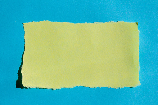 Yellow torn paper on isolated blue background with copy space. Blank ripped paper piece.