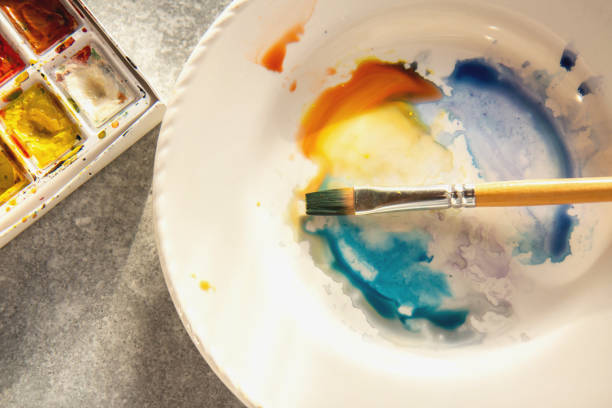 Watercolor paint palette, brush and multicolored paint drops. Close up