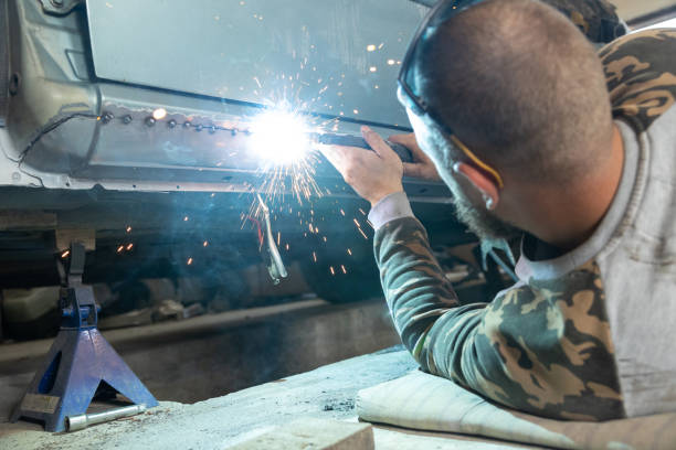 the professional auto mechanic uses a welding machine to repair a car. - car bodywork flash imagens e fotografias de stock