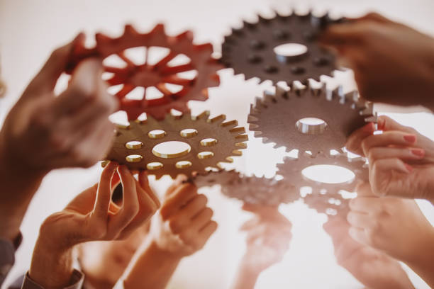 istock People's hands joining different metal cog wheel together. 1682400014