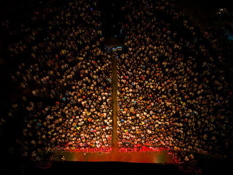 Crowd of people at music concert having fun in front of the stage, red lights illuminate people from the stage, drone photo