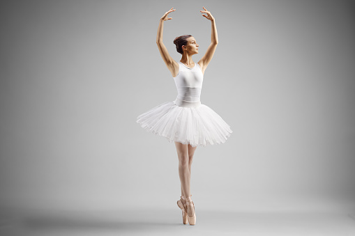 Ballerina in a white dress dancing with arms up isolated on grey background