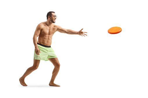 Shirtless man in shorts throwing a plastic disk isolated on white background