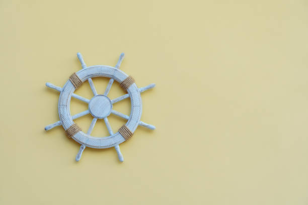 istock White steering wheel helm decorated with rope hanging on wall on yellow background. Wall decoration, sea travelling. 1682435519