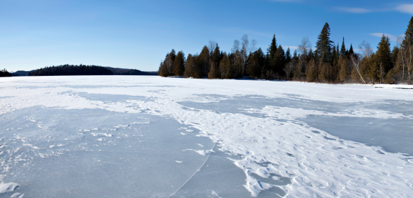 Lanaudiere Quebec frozen lake panorama with snow, an ice crack and a forest.