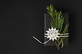 Black craft box with thuja branch and snowflake and white ribbon on a dark background with space for your text