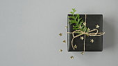 Black gift box with thuja and confetti on a gray background. Flatly, copyspace.