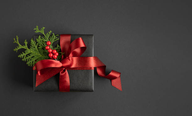 istock Banner with black gift box with red ribbon and thuja on a black background. Top view. Copyspace. 1682483141