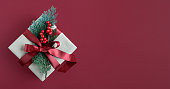 Craft gift box with red ribbon, thuja sprig and berries on red background. Place for your text.
