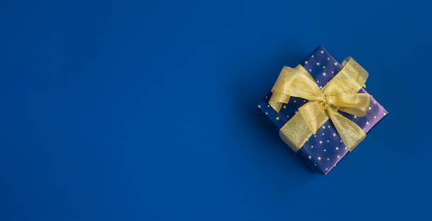 istock Banner with a blue gift box with golden ribbon on blue background. Top view. Space for text. 1682484252