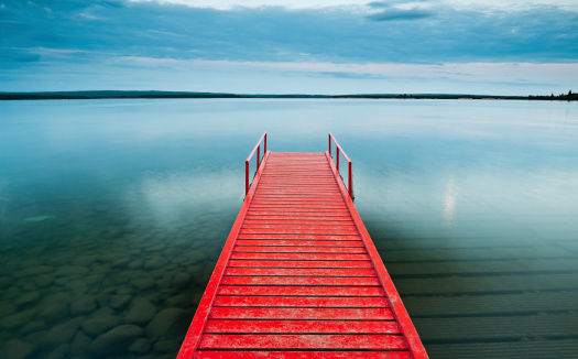 Red dock in Cold Lake Alberta Canada.  3 Photo stitch was taken with a tilt shift lens to create front to back sharp focus of the dock.  Great copy space in the sky and water.