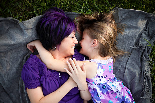 Stylish Mother Laying in Grass with Daughter Laughing Color image of a stylish mother laying in the grass on a blanket with her daughter laughing and bonding. purple hair stock pictures, royalty-free photos & images
