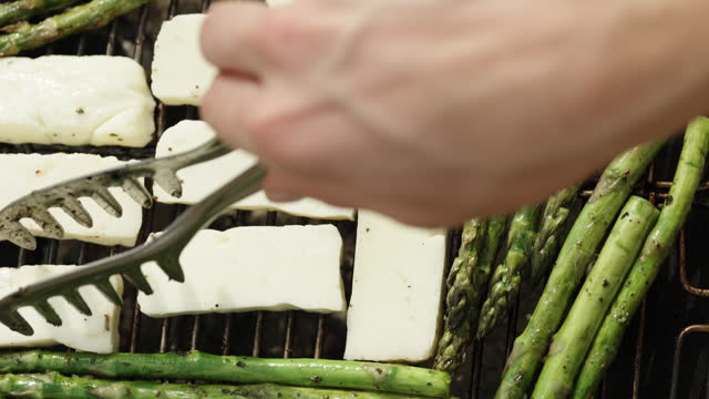 I am flipping the pieces of Haloumi cheese that are being grilled along with the asparagus on the charcoal grill.