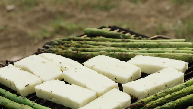 Haloumi cheese is being grilled on a mini charcoal grill along with asparagus.