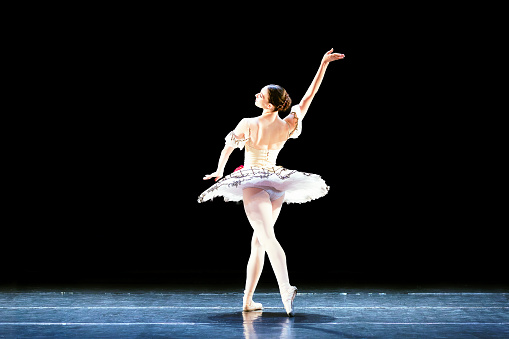 Prima ballerina white swan on the stage gracefully dancing on decorative theatrical background.