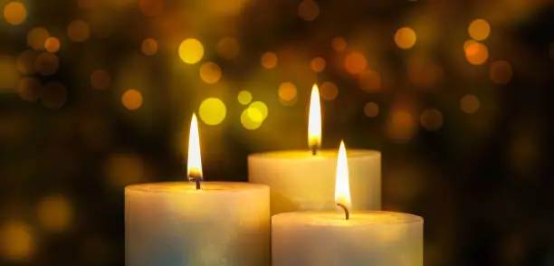three burning candlelights on abstract blurred bokeh light background, golden bright color for warm festive atmosphere, holiday celebration concept