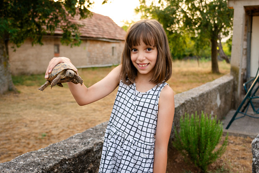 A happy girl is holding a turtle in the yard and looking at camera