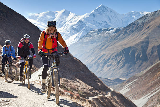Female mountainbike leader on Annapurna Circuit, Nepal A female mountainbiker is leading a group on their ascend towards Thorong La (5.416 mt, 17.770 ft), the highest point on the Annapurna Circuit, Nepal. This trekking route is one of the most famous trails in the world. The bikers are above 3.500 mt (11.500 ft) altitude; the summits of the Annapurna range in the background are above 7.000 mt (23.000 ft). annapurna conservation area photos stock pictures, royalty-free photos & images