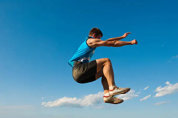 Side view of young male athlete at long jump against the blue sky