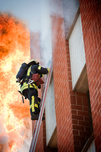 Fully equipped firefighter on a ladder - in the background a huge jet of flame