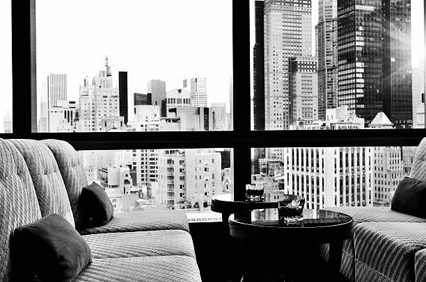  Window inside a bar lounge. There are two sofa and two small coffee tables. On the tables there are flowers in a bowl. Out of the window there is a panoramic view of Upper Midtown Manhattan, NYC.