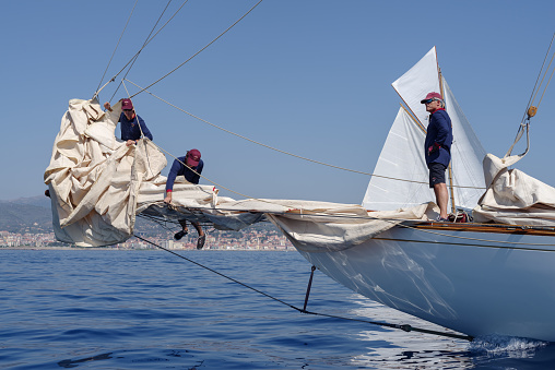 Imperia, Italy - September 10, 2023: Crew members aboard on sailboat Tuiga, flagship of the Monaco Yacht Club, during racing in Gulf of Imperia. Established in 1986, the Imperia Vintage Yacht Challenge Stage is a of the most important event in sailing the Mediterranean dedicated to historical boats