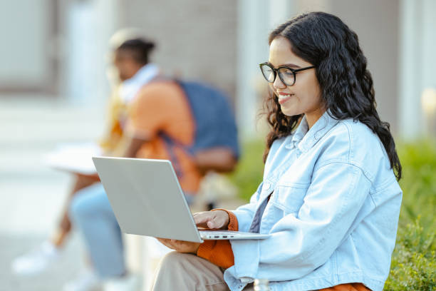 istock Young Latin female student using laptop on the bench on campus 1682543509