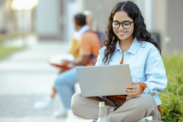 istock Young Latin female student using laptop on the bench on campus 1682544095