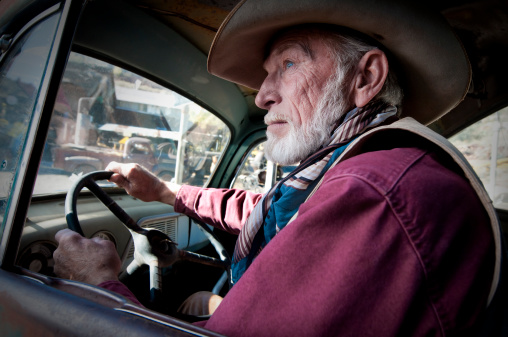 An old cowboy is driving a old, run-down pick up truck.