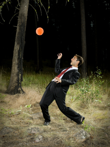 Young man in suit and tie falls backward to avoid falling ball.