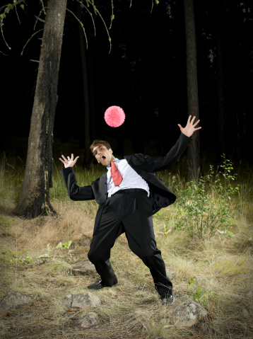 Young man in suit and tie dodges ball in dark forest.