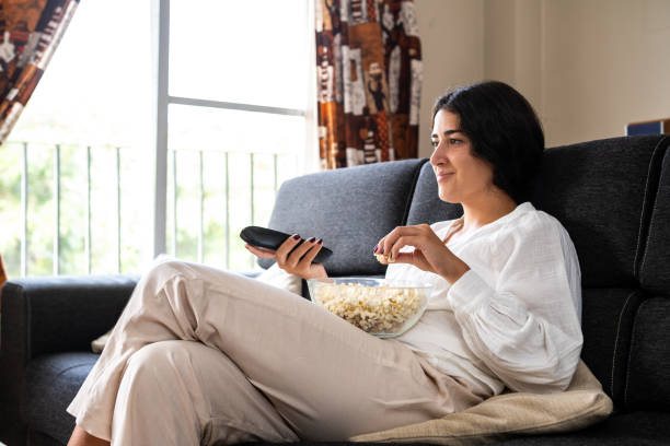 istock A young woman has prepared popcorn and searches for a program on TV with the remote control from her living room sofa. 1682572973
