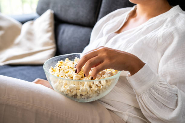 Detail of a young woman eating popcorn on the sofa in her living room. stock photo
